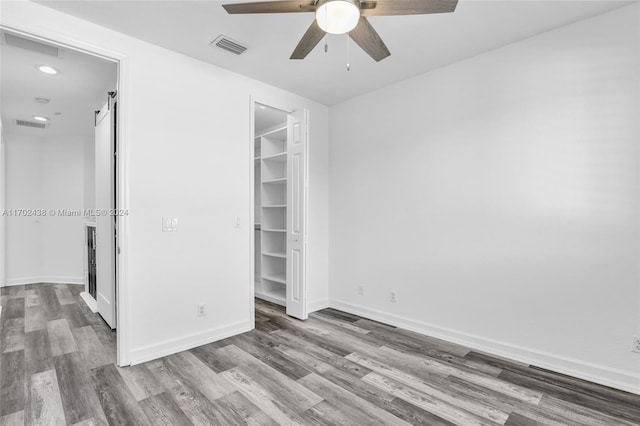 unfurnished bedroom featuring a barn door, hardwood / wood-style flooring, a spacious closet, and ceiling fan