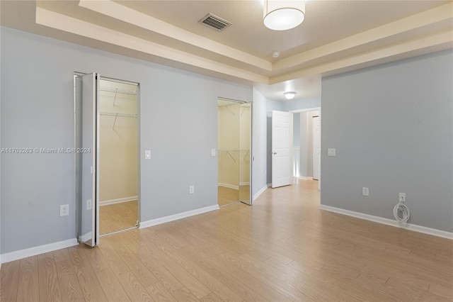 unfurnished bedroom featuring light hardwood / wood-style floors, a raised ceiling, and a walk in closet