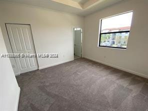 unfurnished bedroom featuring carpet floors, a tray ceiling, and baseboards