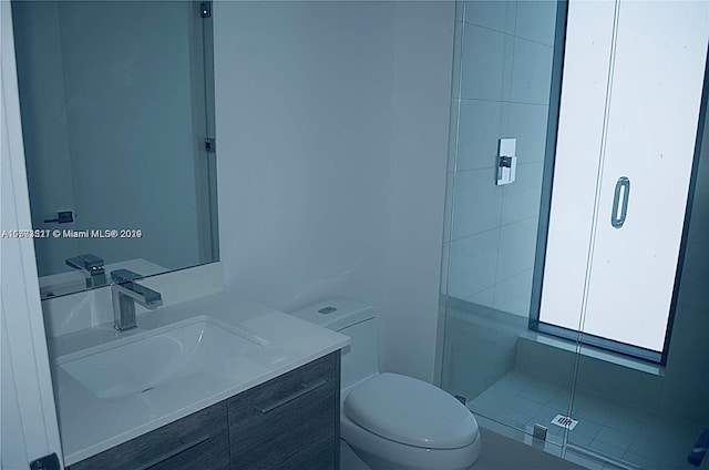 bathroom featuring a shower with door, vanity, and toilet