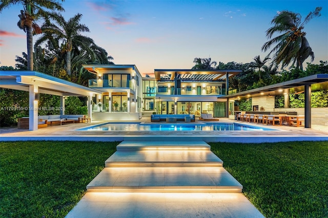 back house at dusk featuring a yard, a swimming pool with hot tub, a balcony, and an outdoor hangout area