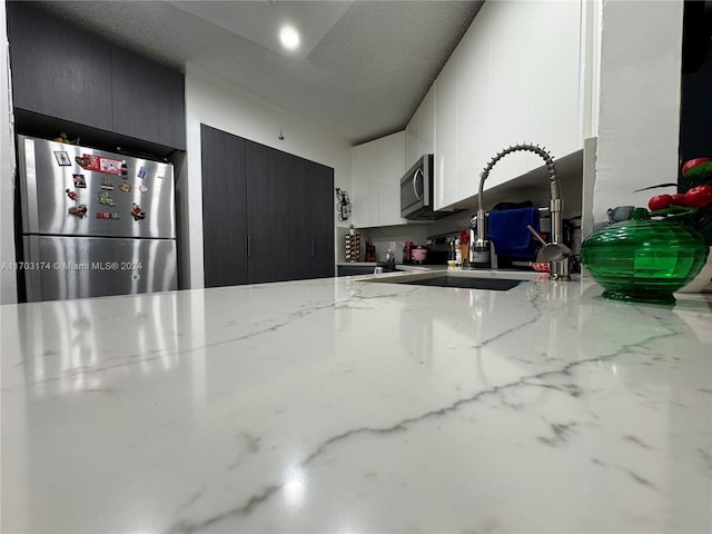 kitchen with light stone counters, sink, a textured ceiling, and appliances with stainless steel finishes