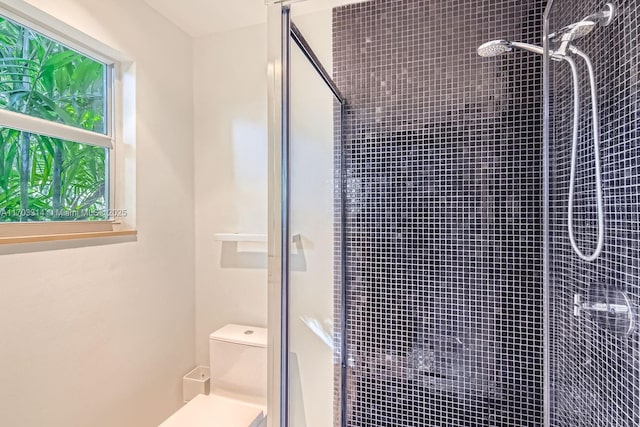 bathroom featuring a wealth of natural light, a shower with door, and toilet