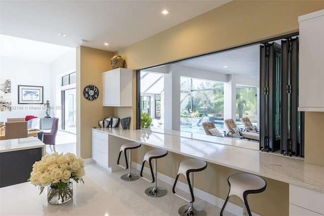 kitchen with a kitchen bar, white cabinets, and light tile patterned flooring