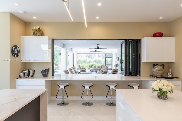 kitchen with a kitchen bar, ceiling fan, white cabinets, and light stone counters