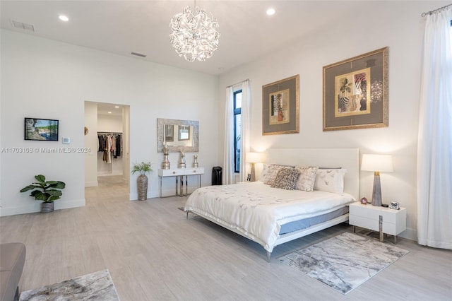 bedroom with a spacious closet, a notable chandelier, and light wood-type flooring