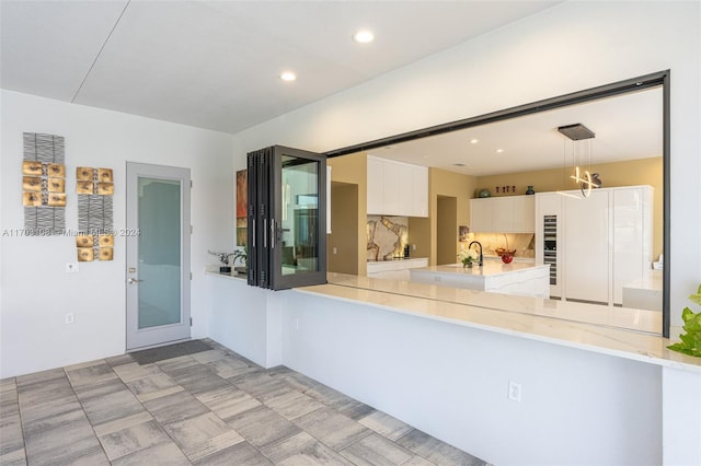 kitchen featuring sink, backsplash, kitchen peninsula, decorative light fixtures, and white cabinets