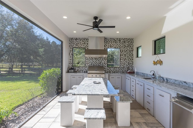 kitchen with a center island, sink, wall chimney exhaust hood, light stone counters, and white cabinetry