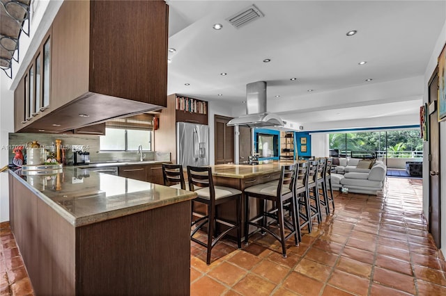 kitchen with a breakfast bar area, island exhaust hood, stainless steel fridge with ice dispenser, and a wealth of natural light