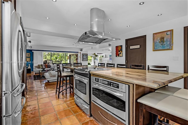 kitchen with dark brown cabinets, a kitchen island, a kitchen bar, island exhaust hood, and stainless steel appliances