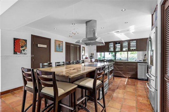 kitchen featuring a breakfast bar, a kitchen island, appliances with stainless steel finishes, island range hood, and dark brown cabinetry