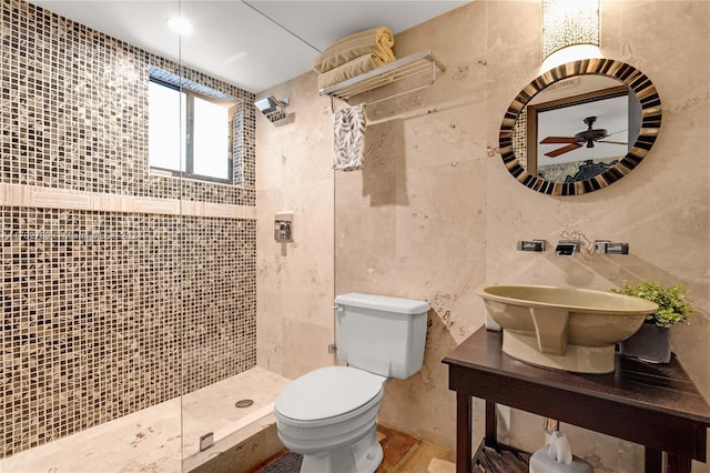 bathroom with ceiling fan, sink, tiled shower, tile walls, and toilet