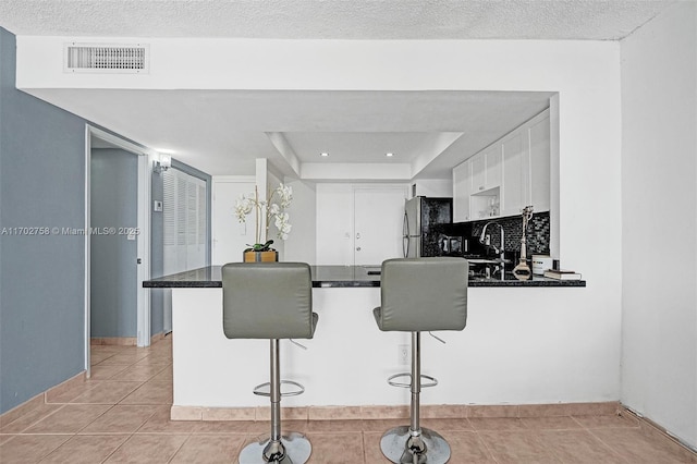 kitchen featuring a breakfast bar area, stainless steel fridge, a tray ceiling, kitchen peninsula, and white cabinets