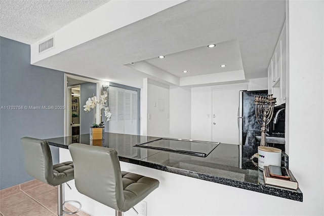 kitchen with a breakfast bar area, white cabinetry, black electric stovetop, a textured ceiling, and a raised ceiling