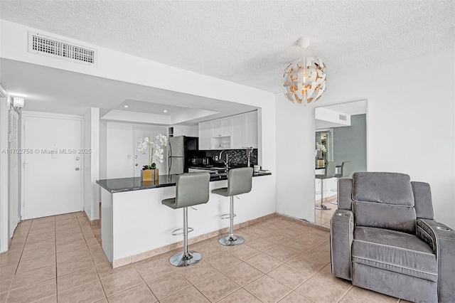 kitchen featuring fridge, light tile patterned floors, white cabinets, and a kitchen bar