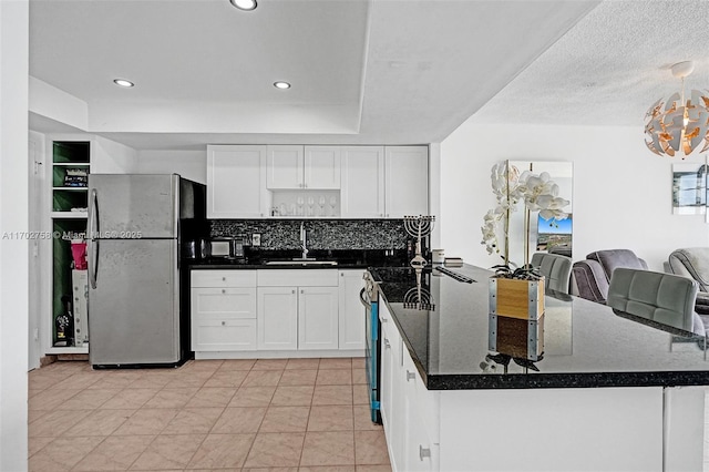 kitchen with decorative light fixtures, sink, white cabinets, stainless steel fridge, and range