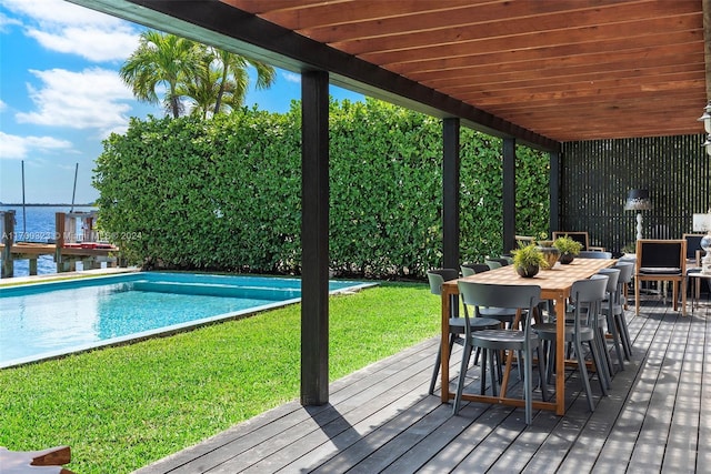 wooden deck featuring outdoor dining area, a water view, an outdoor pool, and a lawn