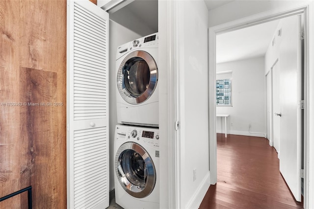 laundry area featuring stacked washer and dryer and dark wood-type flooring