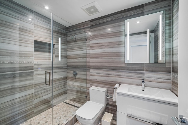 bathroom with a shower with door, vanity, tile walls, and toilet