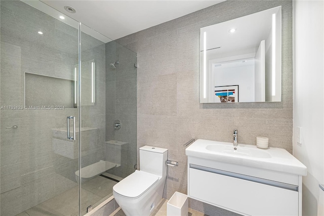 bathroom with vanity, toilet, a shower with door, and tile walls