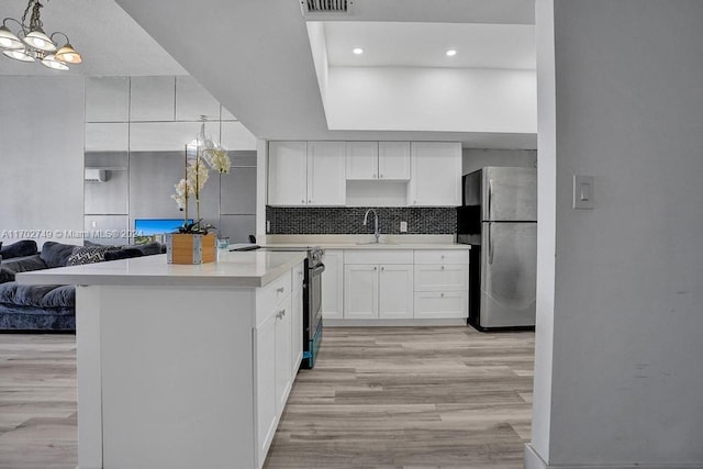 kitchen with white cabinets, sink, stainless steel fridge, black range with electric cooktop, and light hardwood / wood-style floors