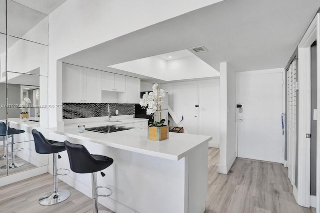 kitchen featuring white cabinetry, tasteful backsplash, kitchen peninsula, light hardwood / wood-style floors, and a breakfast bar area