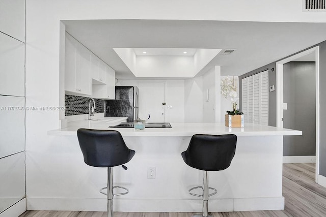 kitchen with a raised ceiling, kitchen peninsula, light hardwood / wood-style flooring, white cabinetry, and a breakfast bar area