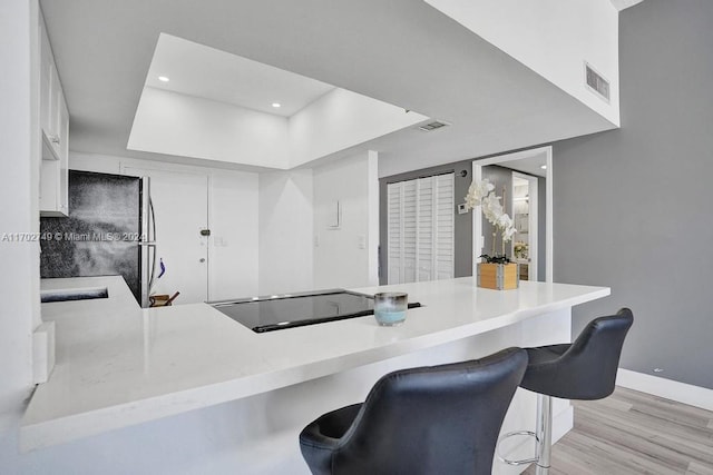 kitchen with a kitchen bar, kitchen peninsula, black fridge, and white cabinetry