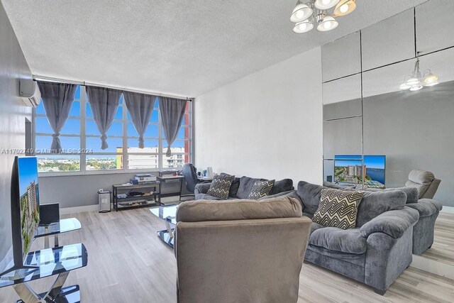 living room featuring a chandelier, a textured ceiling, light wood-type flooring, and an AC wall unit