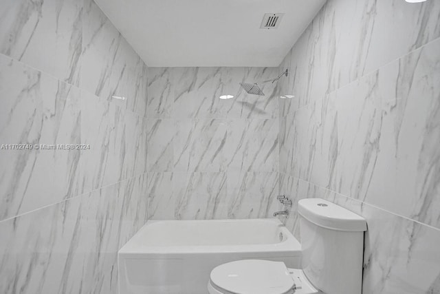 bathroom with tiled shower / bath, toilet, and tile walls