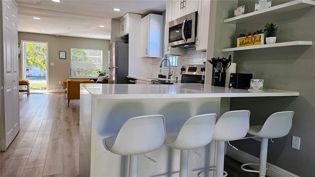 kitchen featuring a kitchen breakfast bar, kitchen peninsula, white cabinetry, and appliances with stainless steel finishes