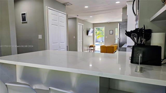 kitchen featuring kitchen peninsula, stainless steel fridge, and light stone countertops