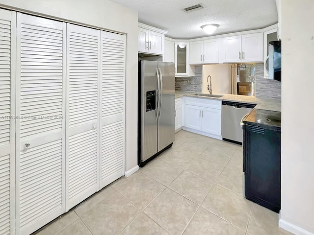 kitchen featuring decorative backsplash, stainless steel appliances, sink, light tile patterned floors, and white cabinets