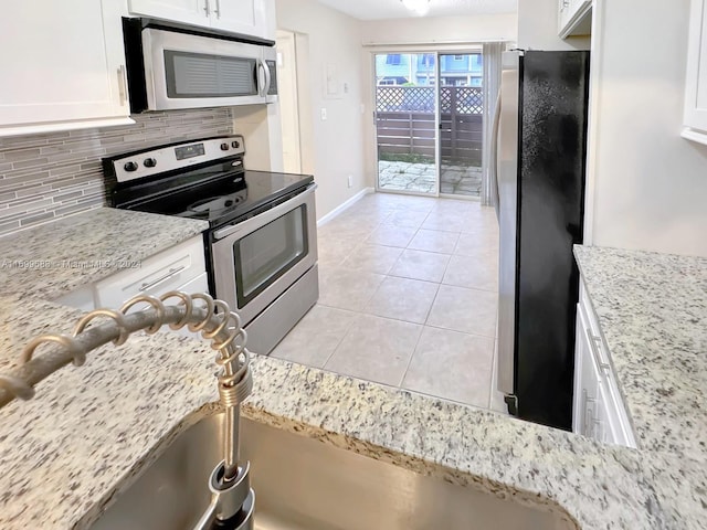 kitchen featuring white cabinetry, stainless steel appliances, tasteful backsplash, light stone counters, and light tile patterned flooring