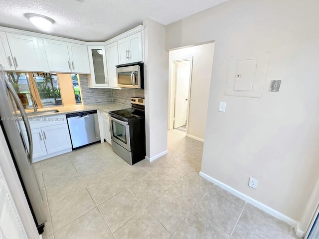 kitchen with appliances with stainless steel finishes, backsplash, a textured ceiling, light tile patterned floors, and white cabinetry