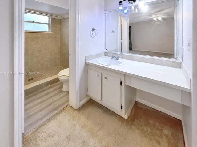 bathroom featuring toilet, wood-type flooring, vanity, and a tile shower