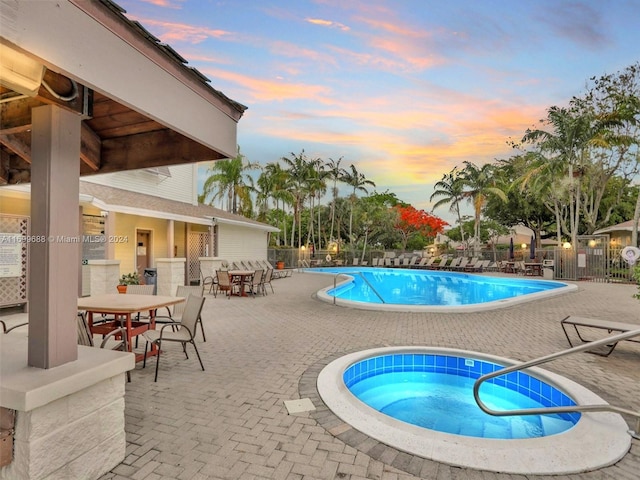 pool at dusk featuring a patio area and a hot tub