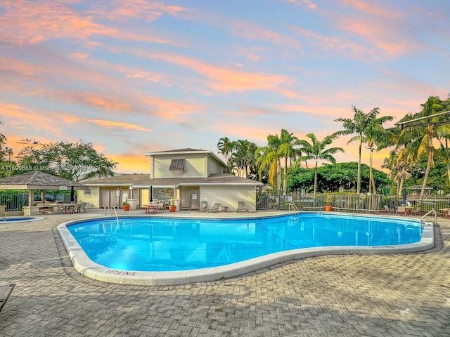 pool at dusk featuring a gazebo and a patio area