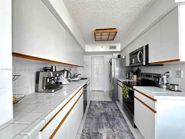 kitchen featuring black appliances, white cabinetry, backsplash, and tile countertops