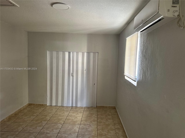 unfurnished room with light tile patterned floors, a textured ceiling, and a wall mounted AC