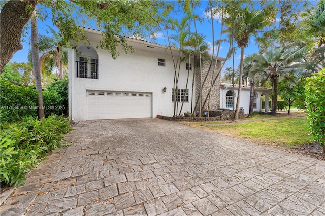 view of front of home with decorative driveway, an attached garage, and stucco siding