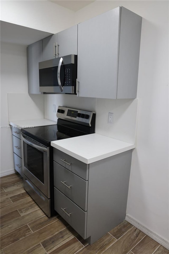 kitchen with gray cabinets, dark wood-type flooring, and appliances with stainless steel finishes