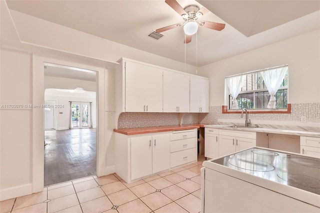 kitchen featuring decorative backsplash, stove, white cabinetry, and sink