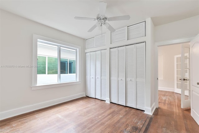 unfurnished bedroom featuring hardwood / wood-style floors, two closets, and ceiling fan