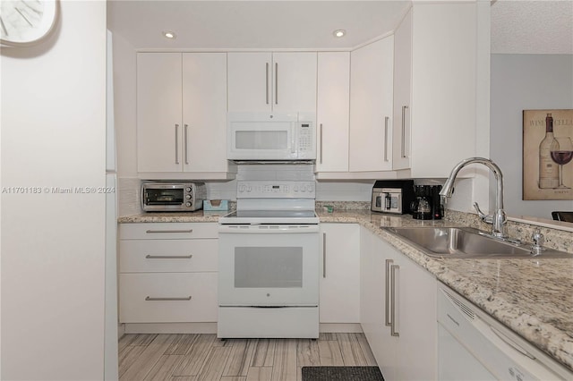 kitchen with white appliances, sink, light wood-type flooring, light stone counters, and white cabinetry