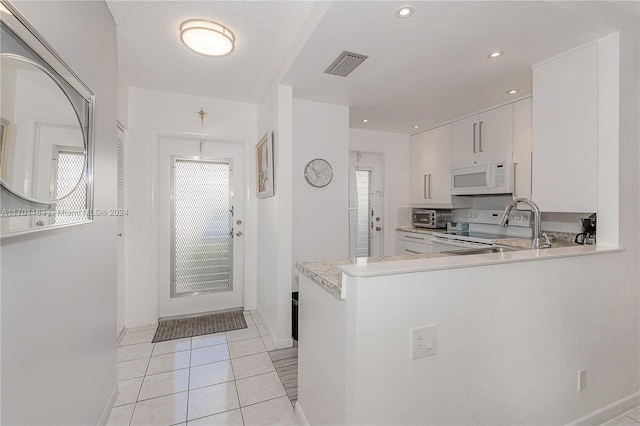 kitchen with electric range, light tile patterned floors, kitchen peninsula, a textured ceiling, and white cabinets