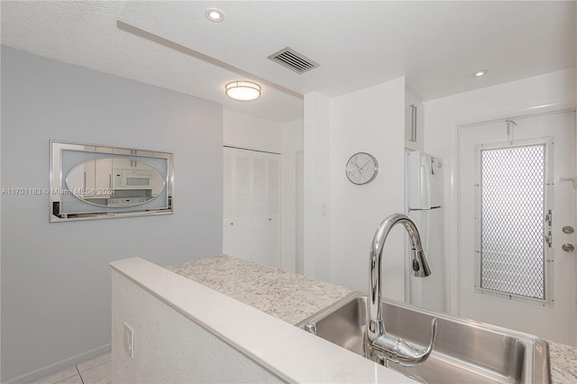 kitchen with a textured ceiling, white appliances, light tile patterned floors, and sink