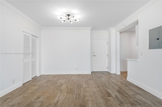 empty room with ornamental molding, an inviting chandelier, electric panel, and light hardwood / wood-style floors