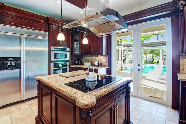 kitchen featuring light stone countertops, appliances with stainless steel finishes, backsplash, a center island with sink, and hanging light fixtures