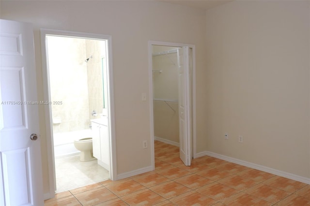 unfurnished bedroom featuring light tile patterned floors, a closet, a spacious closet, and ensuite bath